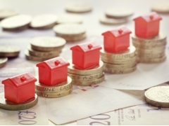 image of Twenty pound bank notes and pound coins with monopoly house on top.